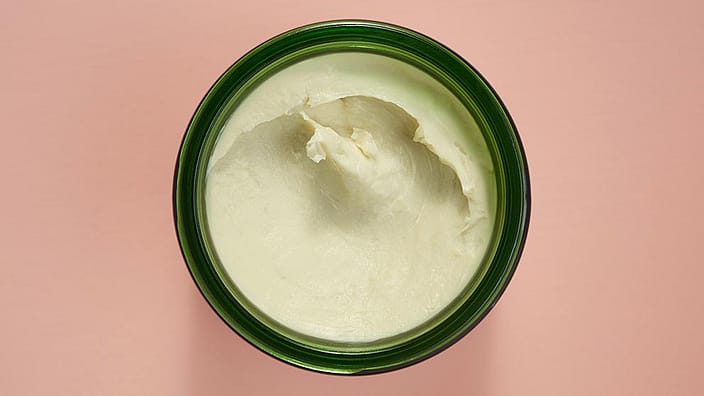 overhead shot of open jar of body butter with pink background